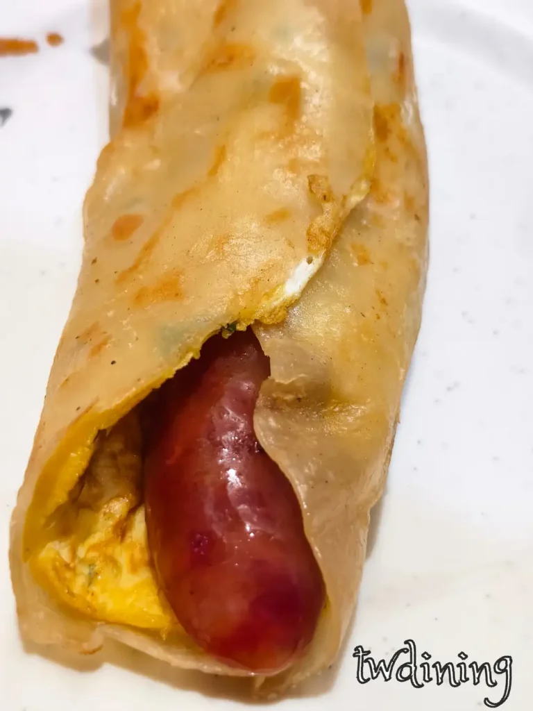 Savory-sausage wrapped in a tender-omelet skin. The egg pancake has flaky-texture edges. 酥軟蛋餅包入多汁香腸，每一口都是 rich-flavor 與 steaming-hot 誘惑，完全展現驢磨坊傳統小吃的視覺精髓。