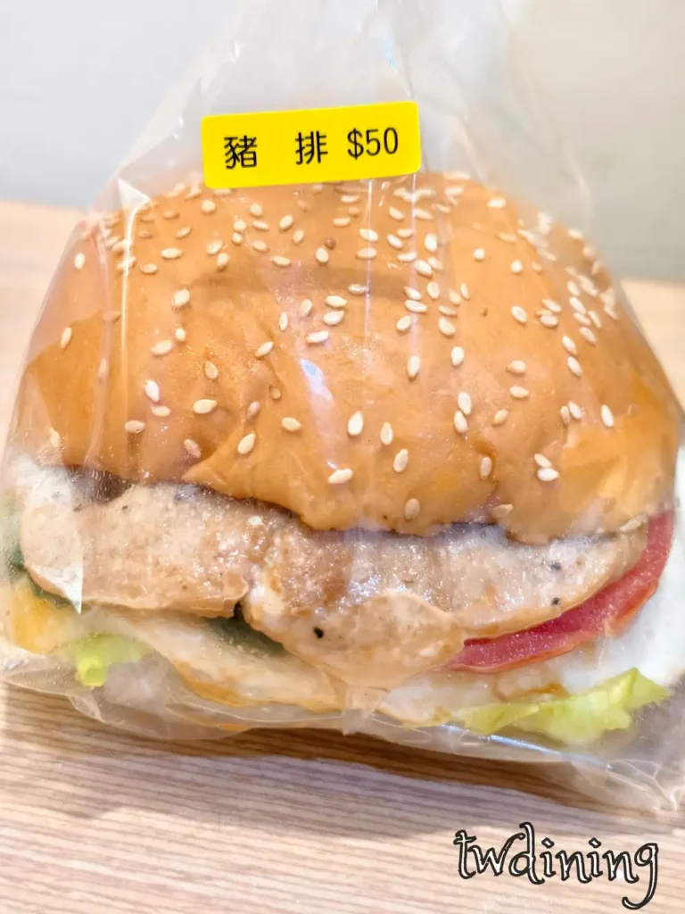 驢磨坊 thick-pork-steak hamburger. The fluffy bun with sesame seeds wraps a succulent-meat patty and fresh tomato. 這顆豬排堡只要 50 元，肉質 tender-juicy 且份量十足，展現台式早餐的 visual essence.