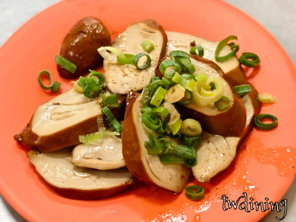 郭家水餃滷素雞切片。入味褐色滷汁素雞搭配大量鮮甜青蔥。橘盤盛裝台式滷味盤。特寫呈現柔軟紮實孔洞吸附湯汁視覺感。多汁素食滷味細節。