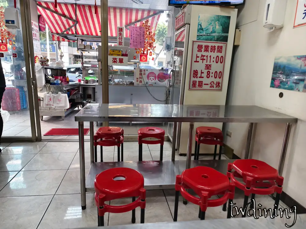 走進郭家水餃室內空間很明亮。不鏽鋼長桌配紅色圓凳。牆上貼著營業時間與自取 menu 告示。呈現台式小吃店特有的親切氛圍。環境簡約乾淨。捕捉日常內用動線與舒適空間細節。這就是在地麵點食趣。
