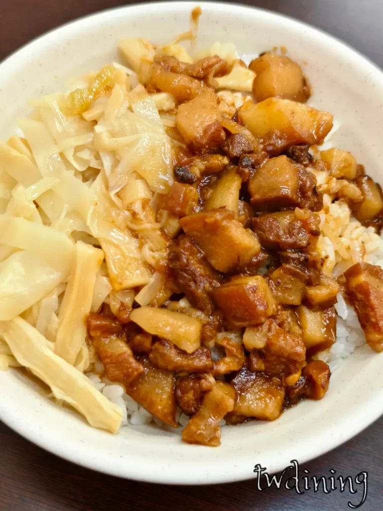 贊鴨手製滷肉飯。深褐色肥瘦均勻的切丁滷肉淋在飽滿白米飯上，搭配側邊鮮嫩黃色滷筍絲配菜，呈現油脂光澤感與台式經典滷汁色澤，精確捕捉國民美食的視覺精髓與豐富食材堆疊層次。